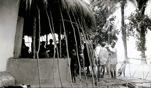 Women plastering and men thatching a community meeting house
